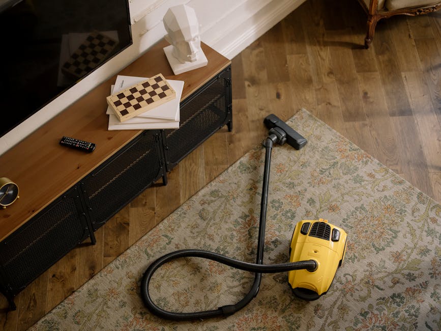 A professional cleaning technician from Dagenham Carpet Cleaners wearing a white protective suit, face mask, and blue gloves, is performing deep cleaning on a plush beige carpet in a bright, modern li